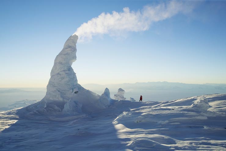 A steaming fumarolic ice tower above "Sauna Cave" at 3,550 meters on Mt. Erebus, Antarctica. Heat from magma (molten rock) in the volcano melts the snow and ice beneath the ice towers forming caves and tunnels. As the air temperatures are typically colder than -30°C the water vapor freezes into towers of ice. At this latitude and altitude, the ice never melts. The towers can grow over 15 meters high until they become unstable and collapse under their own weight or are blown over. Photo was taken near midnight on the week of the last sunset for many months.